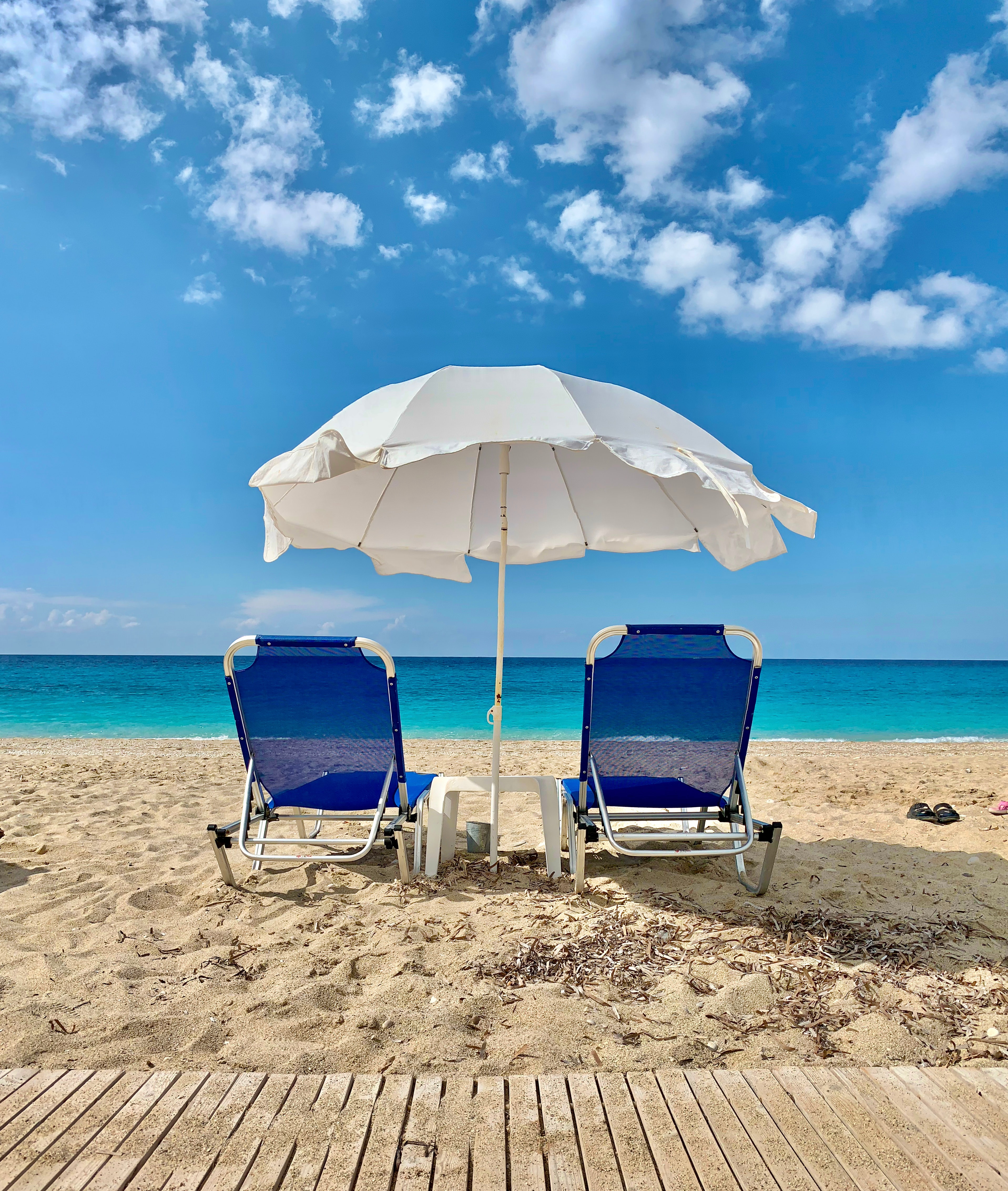 Blaue Liegestühle und weißer Sonnenschirm auf Strand am Meer